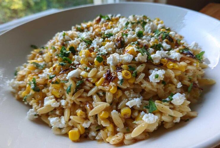 A close-up of Mexican Street Corn Orzo Pasta Salad topped with cotija cheese and cilantro in a white bowl.