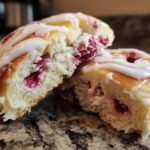 Close-up of a Raspberry Cream Cheese Sweet Roll cut in half showing soft dough, raspberry filling, and vanilla glaze.