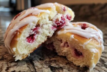 Close-up of a Raspberry Cream Cheese Sweet Roll cut in half showing soft dough, raspberry filling, and vanilla glaze.