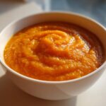 Close-up of vibrant orange Roasted Apple Pumpkin Soup, swirled texture, served in a white bowl.