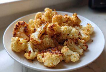 A close-up of crispy, golden brown Roasted Cauliflower Bites piled high on a white plate.
