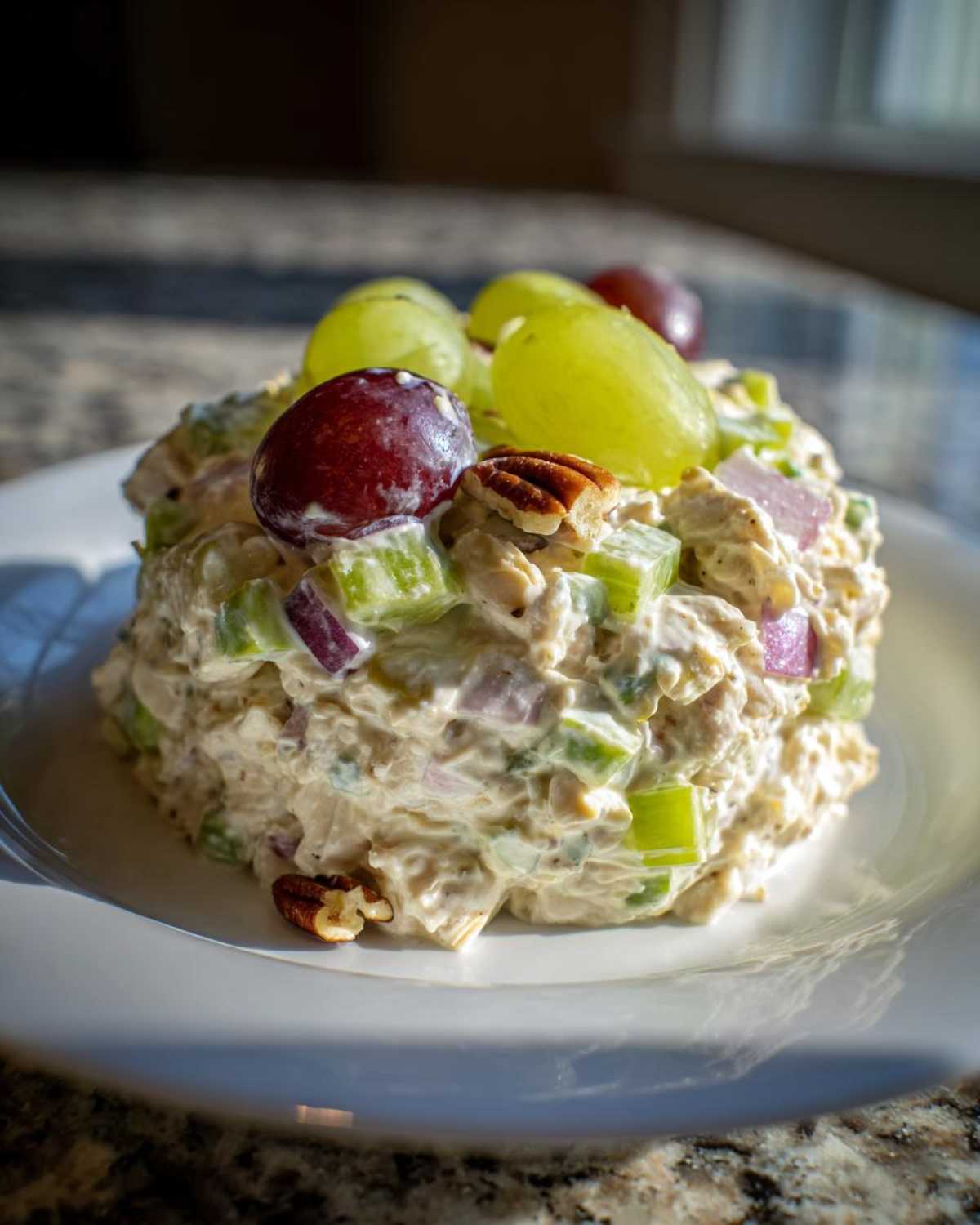 A molded serving of The Chicken Salad mixed with celery and red onion, topped with red and green grapes and pecans.