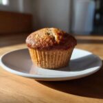 A single, perfectly baked Vanilla Chai Muffin with a golden brown, slightly cracked top, resting on a small white plate.