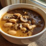 Close-up of a white bowl filled with rich Vegan Stew with White Beans and Mushrooms, seasoned with herbs.