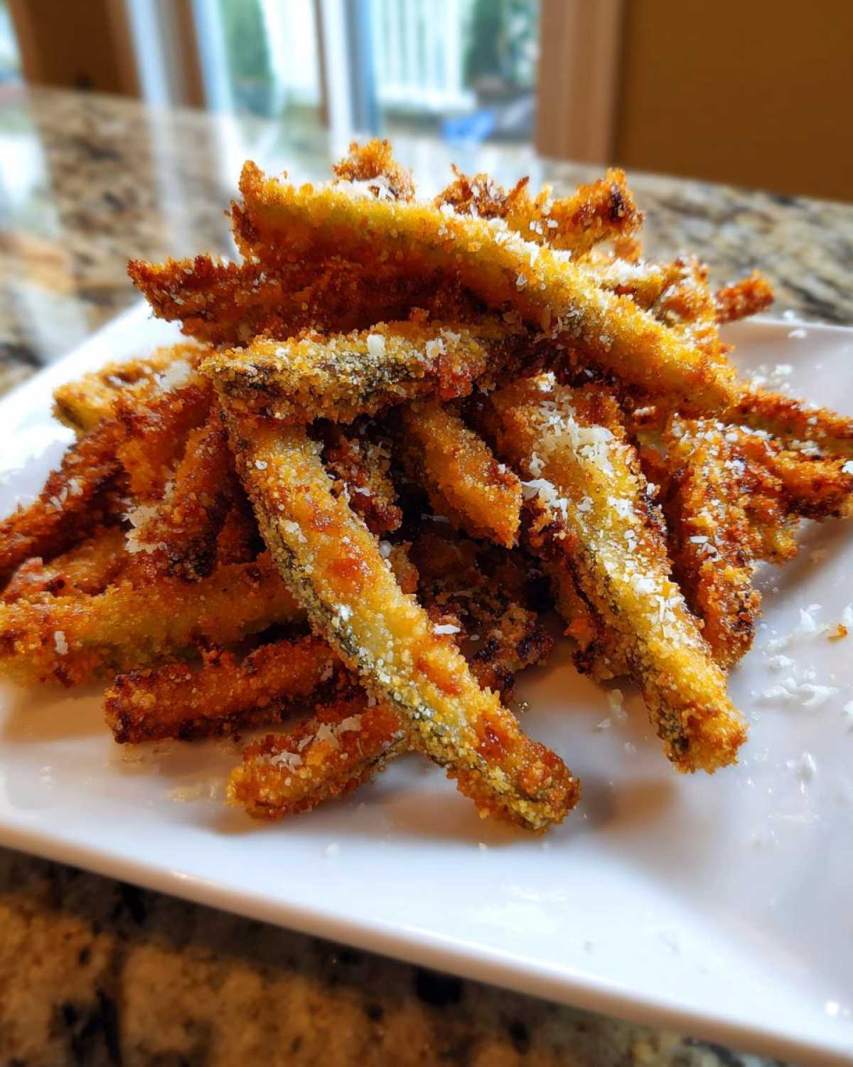 A pile of crispy, golden brown Baked Eggplant Fries sprinkled with grated Parmesan cheese on a white plate.