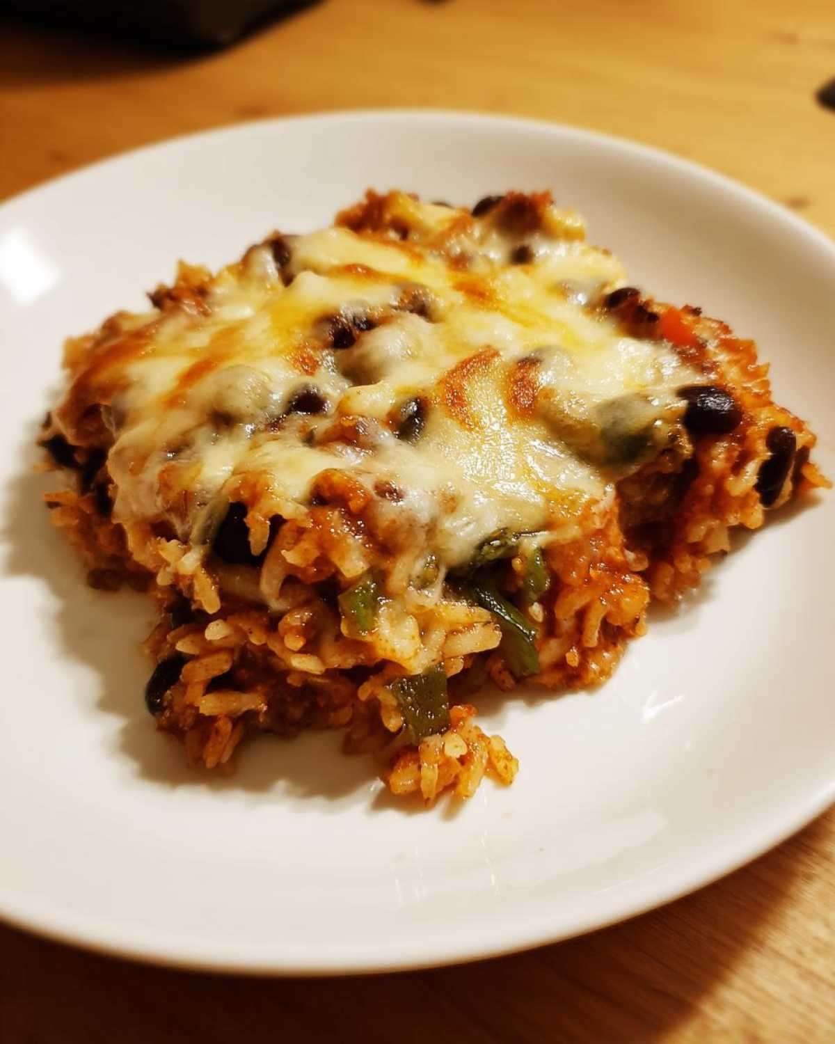 A close-up serving of cheesy Black Bean and Rice Bake topped with melted, golden cheese on a white plate.