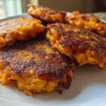 Close-up of several golden brown, pan-fried Chickpea and Sweet Potato Fritters stacked on a white plate.
