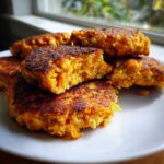 A stack of golden brown, pan-fried Chickpea and Sweet Potato Fritters on a white plate, one broken open to show the texture.