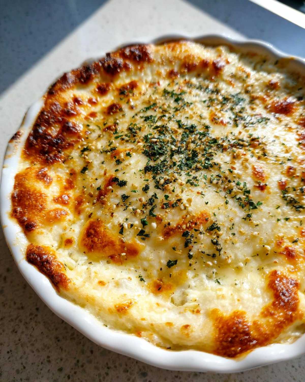 Close-up of a bubbling, golden-brown Creamy Baked Pickle Dip topped with herbs in a white baking dish.