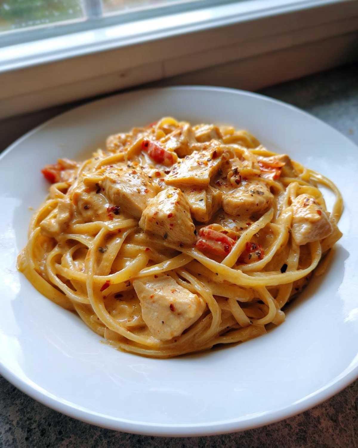 A close-up of creamy Cajun Chicken Pasta featuring linguine noodles, diced chicken, and red peppers, sprinkled with spices.