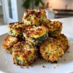 A stack of golden brown, crispy Air Fryer Zucchini Bites sprinkled with salt and herbs on a white plate.