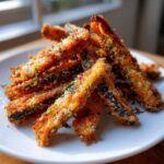 A pile of golden brown, crispy Baked Eggplant Fries dusted with Parmesan cheese and herbs on a white plate.