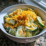 A close-up of Cucumber Ranch Crack Salad featuring sliced cucumbers in a creamy dressing, topped with shredded cheddar cheese and breadcrumbs.