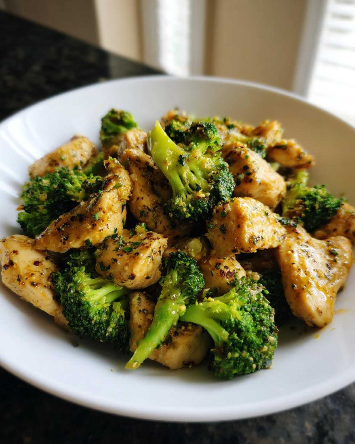 Close-up of bite-sized pieces of Garlic Butter Chicken and Broccoli tossed in a savory sauce, served in a white bowl.
