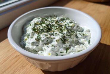 A close-up of creamy Homemade Tzatziki Sauce topped with fresh dill in a white bowl.