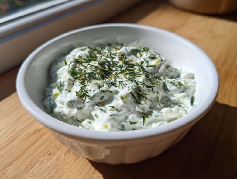 A close-up of creamy Homemade Tzatziki Sauce topped with fresh dill in a white bowl.