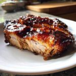 Close-up of tender Honey Garlic Pork coated in a thick, glossy, dark glaze, showing the moist interior.