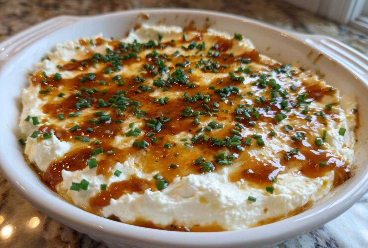 A round white baking dish filled with creamy Hot Honey Ricotta Dip, drizzled with honey and topped with fresh chives.