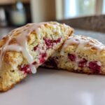 Two halves of a freshly baked Lemon Raspberry Scones, drizzled with thick white icing, showing the bright red raspberries inside.