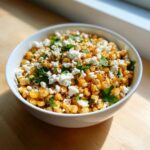 Close-up of a white bowl filled with Mexican Street Corn Salad Esquites, topped generously with crumbled white cheese and fresh cilantro.