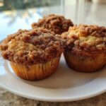 Three moist Coffee Cake Muffins with a thick, sugary cinnamon crumb topping served on a white plate.