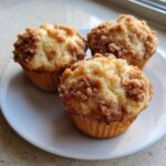 Three freshly baked Coffee Cake Muffins topped with a thick, crumbly cinnamon streusel, resting on a white plate.