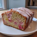 A close-up of a slice of moist Rhubarb Bread topped with a white vanilla glaze, served on a white plate.