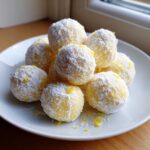 A pile of bright yellow No Bake Lemon Truffles dusted heavily with powdered sugar and lemon zest.