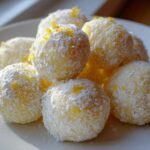 A pile of bright yellow No Bake Lemon Truffles coated in powdered sugar and topped with lemon zest.