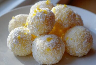 A pile of bright yellow No Bake Lemon Truffles coated in powdered sugar and topped with lemon zest.