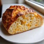 Close-up of a slice showing the airy crumb and melted cheddar pieces in the No Knead Cheddar Bread.