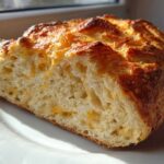 Cross-section of No Knead Cheddar Bread showing airy crumb studded with melted cheese and a golden, crusty top.