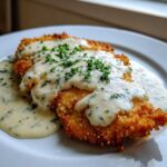 Close-up of crispy, breaded Parmesan Chicken smothered in creamy garlic sauce and topped with fresh parsley.