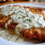 Close-up of crispy, golden Parmesan Chicken smothered in a rich, creamy garlic sauce topped with fresh parsley.