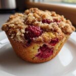 A single, perfectly baked Raspberry Streusel Muffin topped with golden brown streusel sits on a white plate.