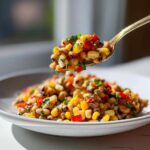 A golden spoon lifting a bite of colorful Cowboy Caviar, featuring black-eyed peas, corn, and red peppers.