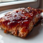 Close-up of a perfectly cooked fillet of Strawberry Balsamic Glazed Salmon covered in a thick, shiny, dark red glaze.