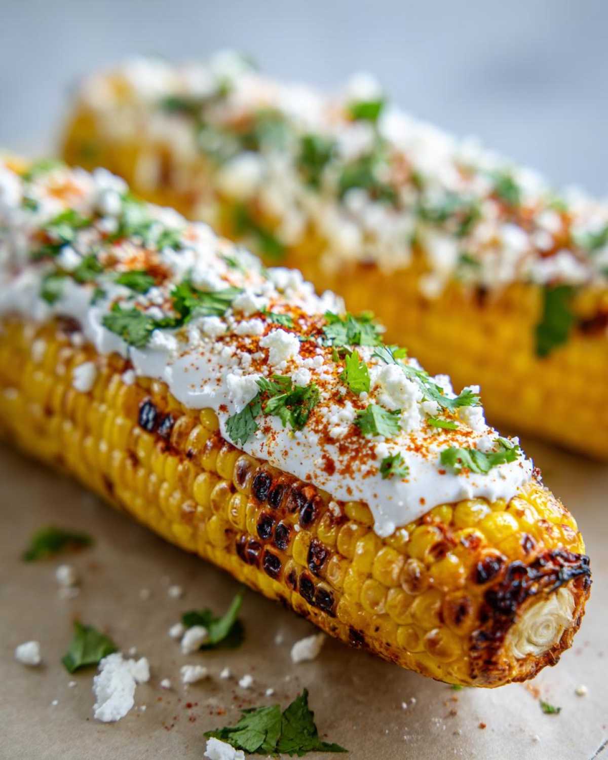 A close-up of grilled Street-Style Mexican Corn on the Cob topped with crema, cotija cheese, chili powder, and cilantro.