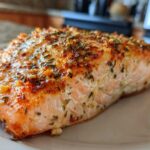 Close-up of a juicy, seasoned fillet of Texas Roadhouse Style Baked Salmon on a white plate.